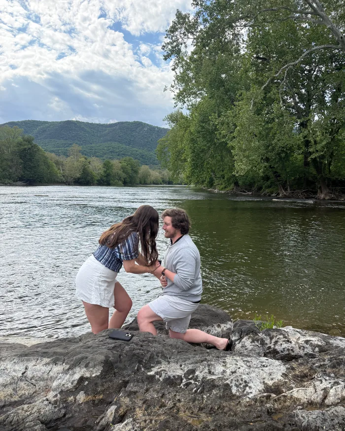Johnny proposing to Isabella on the rocks in the Shenandoah River, mountains in the background